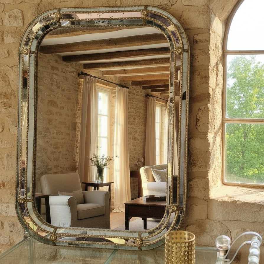 NITUSH Venetian style mirror with ornate bevelled frame and decorative gold accents. Reflects a rustic room with stone walls and wooden beams.